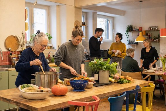 Unverbindliche KI-Konzeptvisualisierung einer warmen Gemeinschaftsküche, in der ältere und jüngere Nachbarn zusammen kochen.